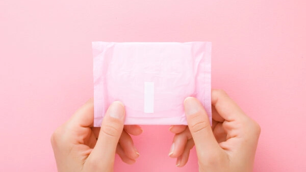 Young woman hands holding pack of sanitary towel on light pink table background. Pastel color. Closeup. Point of view shot. Top down view.