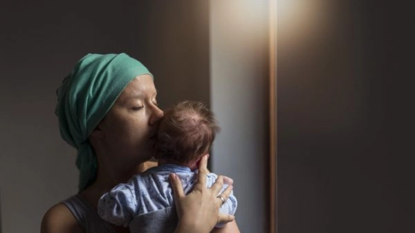 Photo of Female cancer patient holding her baby son next to the window