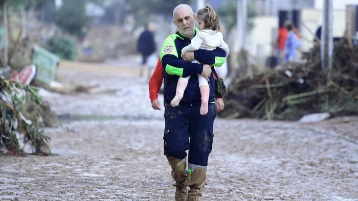 Un volontario della Protezione Civile tiene in braccio una bambina in una strada ricoperta di fango in una zona allagata vicino a Valencia. (AFP)