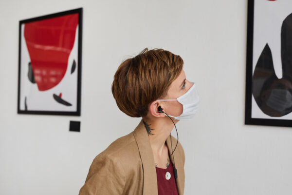 Side view portrait of young woman looking at paintings and wearing mask at modern art gallery exhibition, copy space