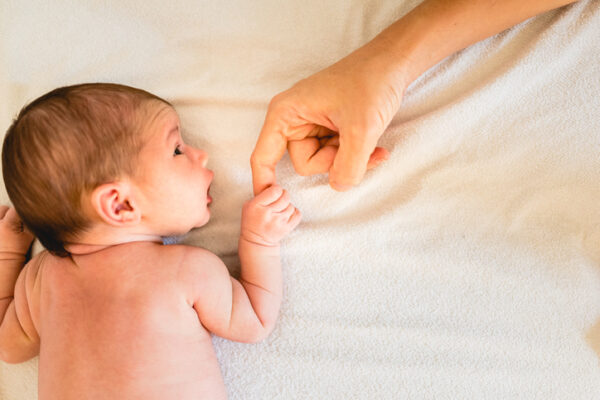 Newborn baby securely grasping his mother's hands, close-up fingers.