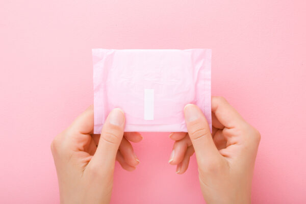 Young woman hands holding pack of sanitary towel on light pink table background. Pastel color. Closeup. Point of view shot. Top down view.