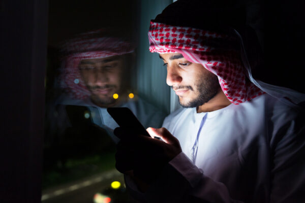 Young Arab messaging his friends at night the plans he has for the next day's desert safari; while standing next to his bedroom window.