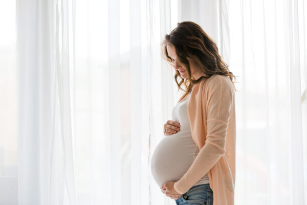 Portrait of young pregnant attractive woman, standing by the window, dressed in casual clothing, day before due date