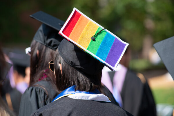 One student stands out from the rest of the graduation crowd in their solid black cap and gowns except for one brave lesbian woman who wears her gay pride colors proudly on her cap.