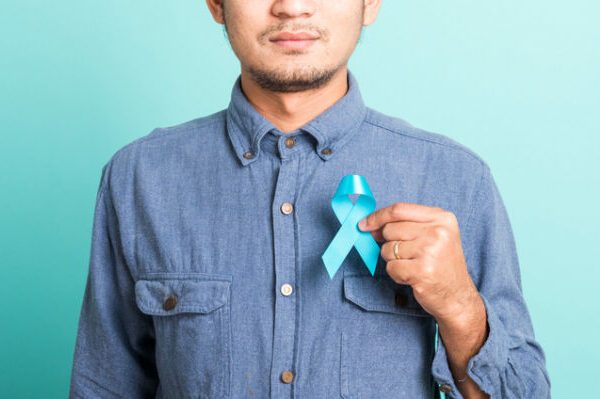 Asian portrait happy handsome man posing he holding light blue ribbon for supporting people living and illness, studio shot isolated on blue background, Prostate Cancer Awareness in November concept