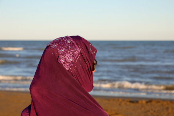 young girl with arabic veil to cover her head by the sea in summer at sunset