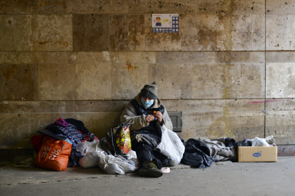 Kyiv, Ukraine - March 18, 2020: Homeless woman in medical mask sits in an underground passage near a closed subway. Due to the coronavirus epidemic, the Ukrainian government has closed the subway.