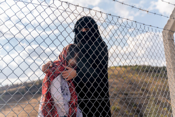 Refugee woman and daughter standing behind a fence