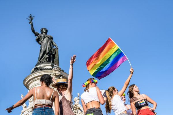 Paris, France - June 29, 2019: Six young women, one waving a rainbow flag high, stand in the sun at the foot of the statue of Marianne on the place de la Republique, where the Gay Pride parade ended.