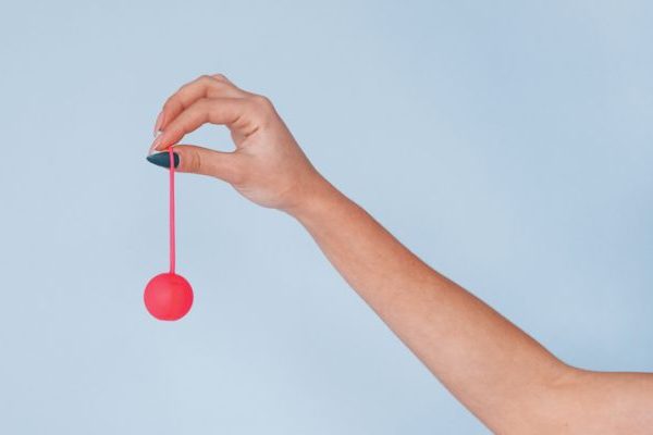 Woman's hands with pink sex ball against studio background.