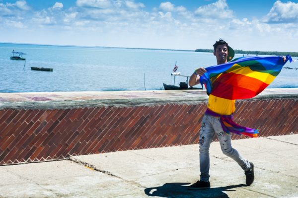 Mazanillo, Cuba - May 15, 2014: A man proudly displays a Gay rainbow flag and struts along the seawall in Manzanillo, Cuba