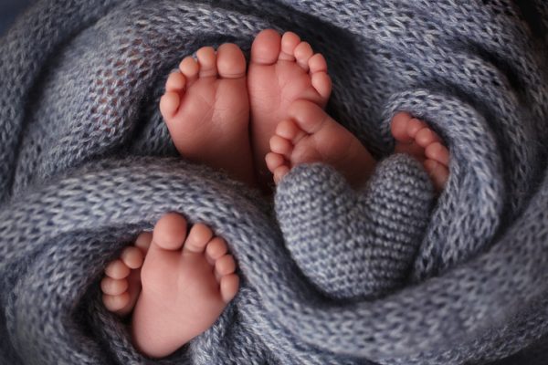 Feet of three newborn babies in a soft blanket. Heart in the legs of newborn triplets. Studio photography. High quality photo